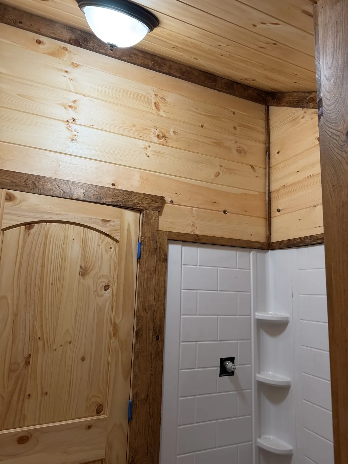 Arched pine door beside a white tile shower surround in a new bathroom