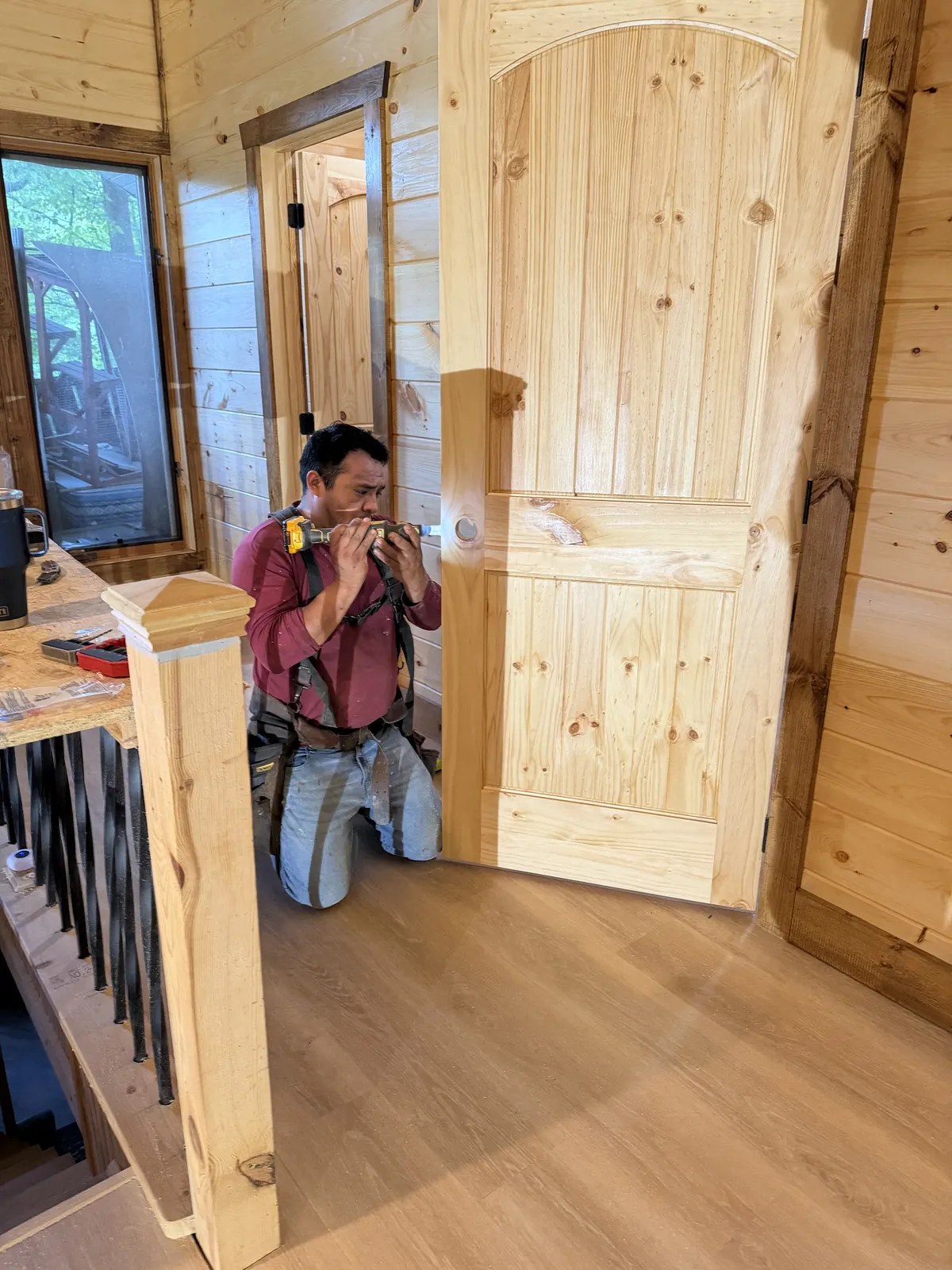 Carpenter hanging an arched knotty pine door beside the stair rail