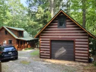 Log garage with a green metal roof beside a cabin