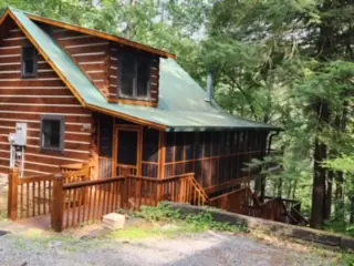 Stained log cabin with a green metal roof and front deck