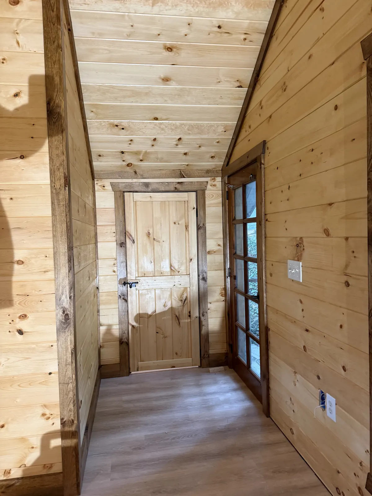 Pine-paneled hallway with a vaulted ceiling and a knotty pine door