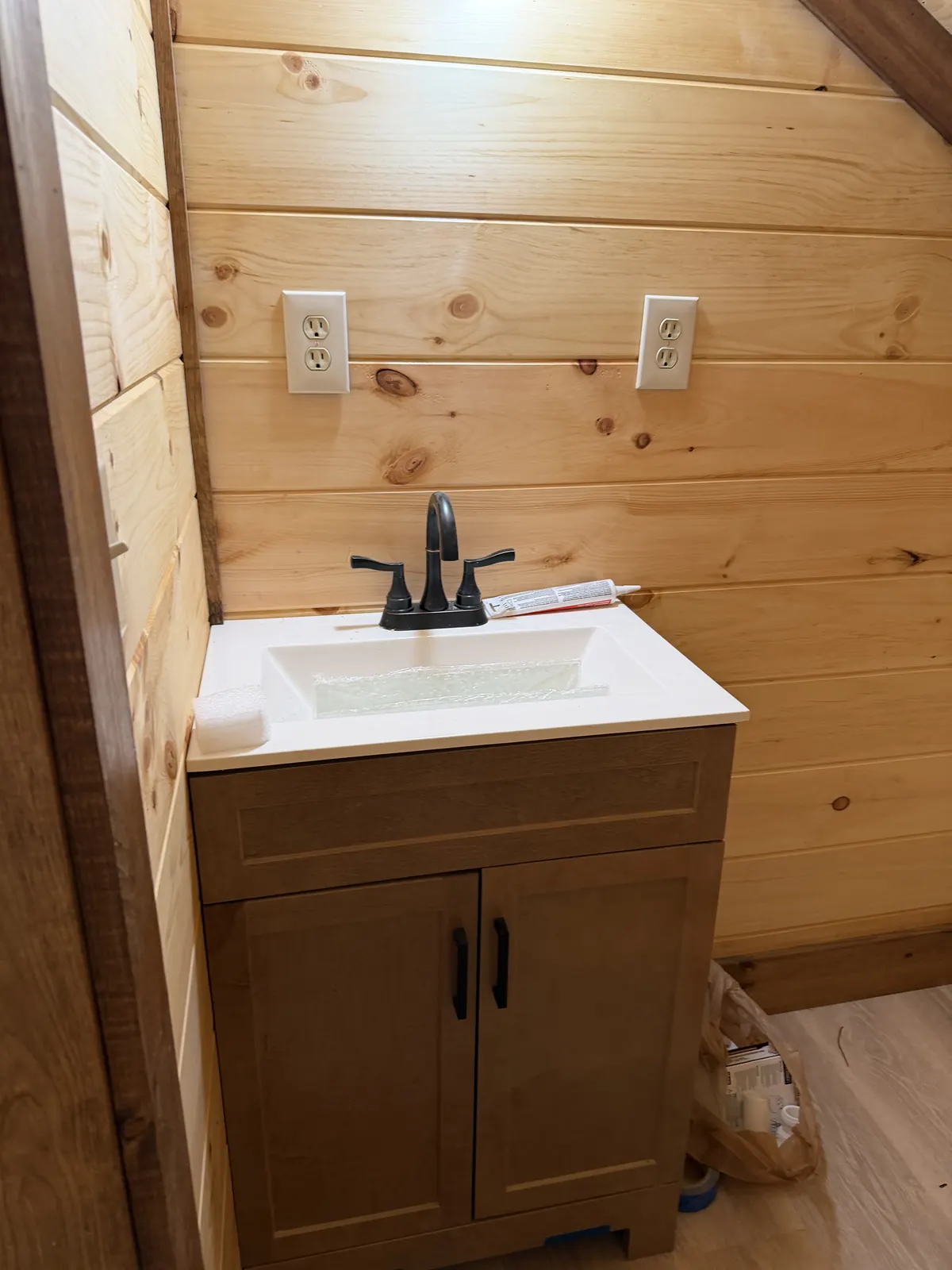 Bathroom vanity with a dark faucet against pine walls