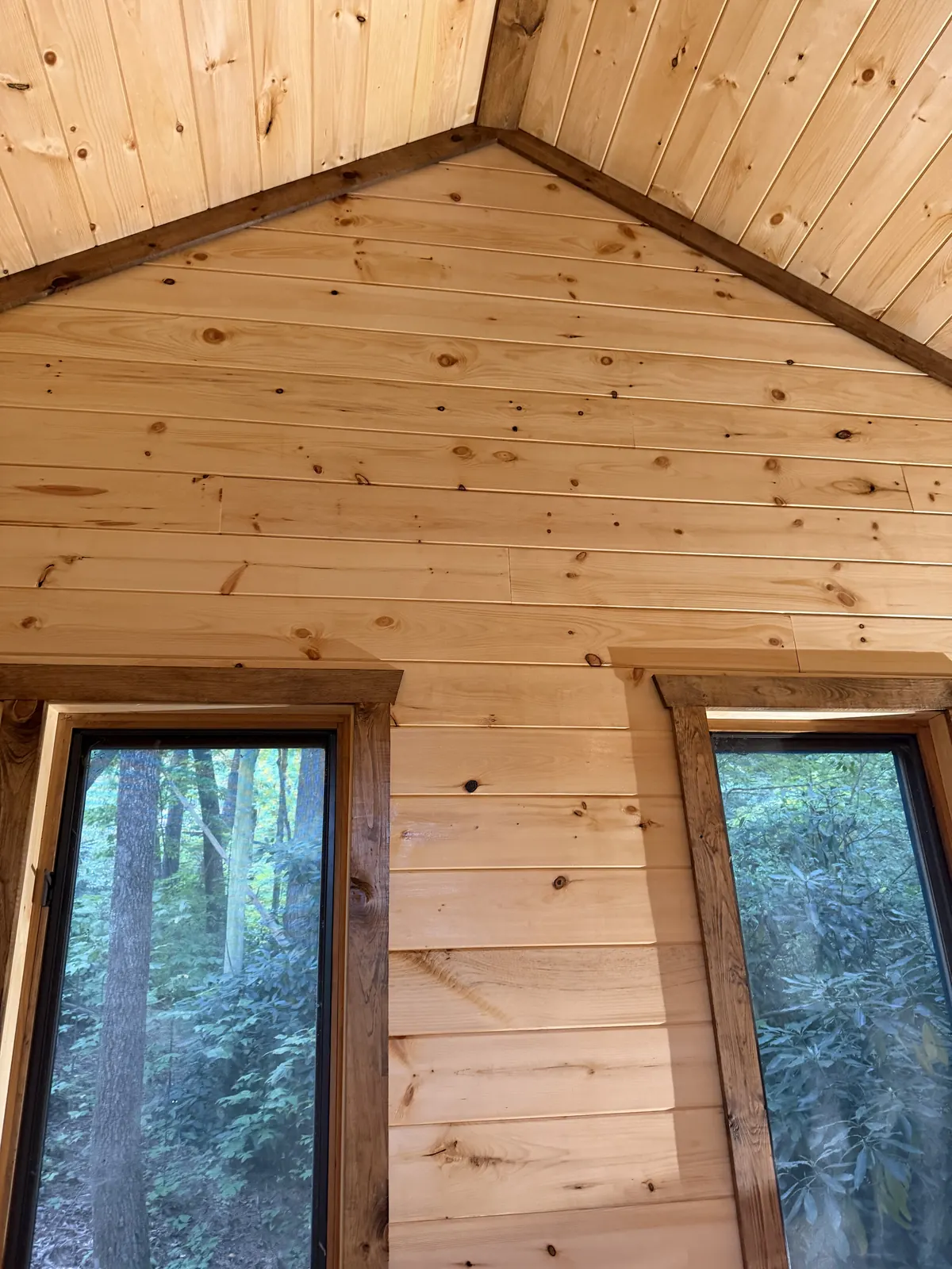 Tall windows trimmed in stained wood in a pine-paneled room