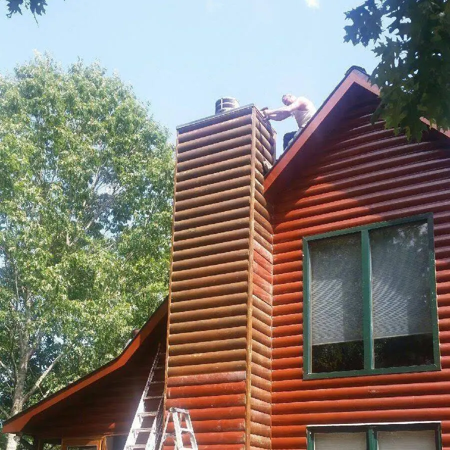 Worker at the top of a log-sided chimney chase on a red-stained home