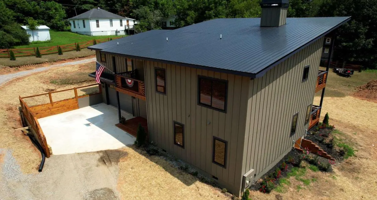 Aerial view of the house with its dark metal roof on a level lot