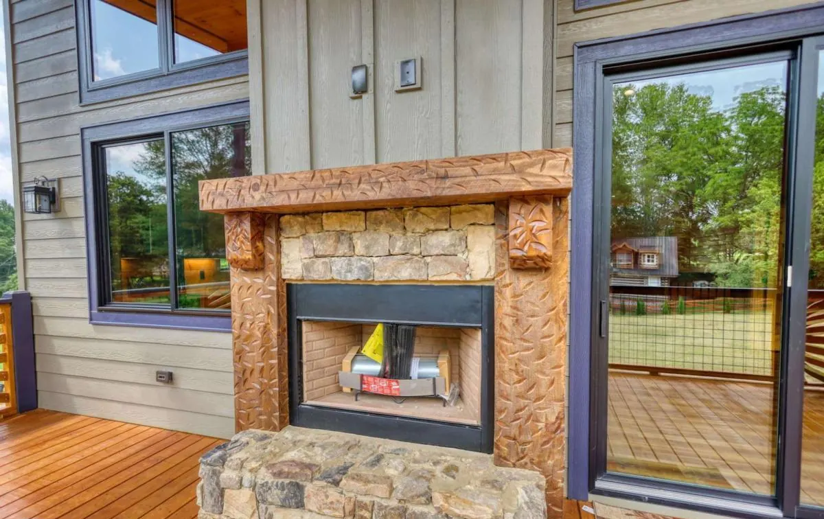 Stone outdoor fireplace with a carved wood surround on the covered porch