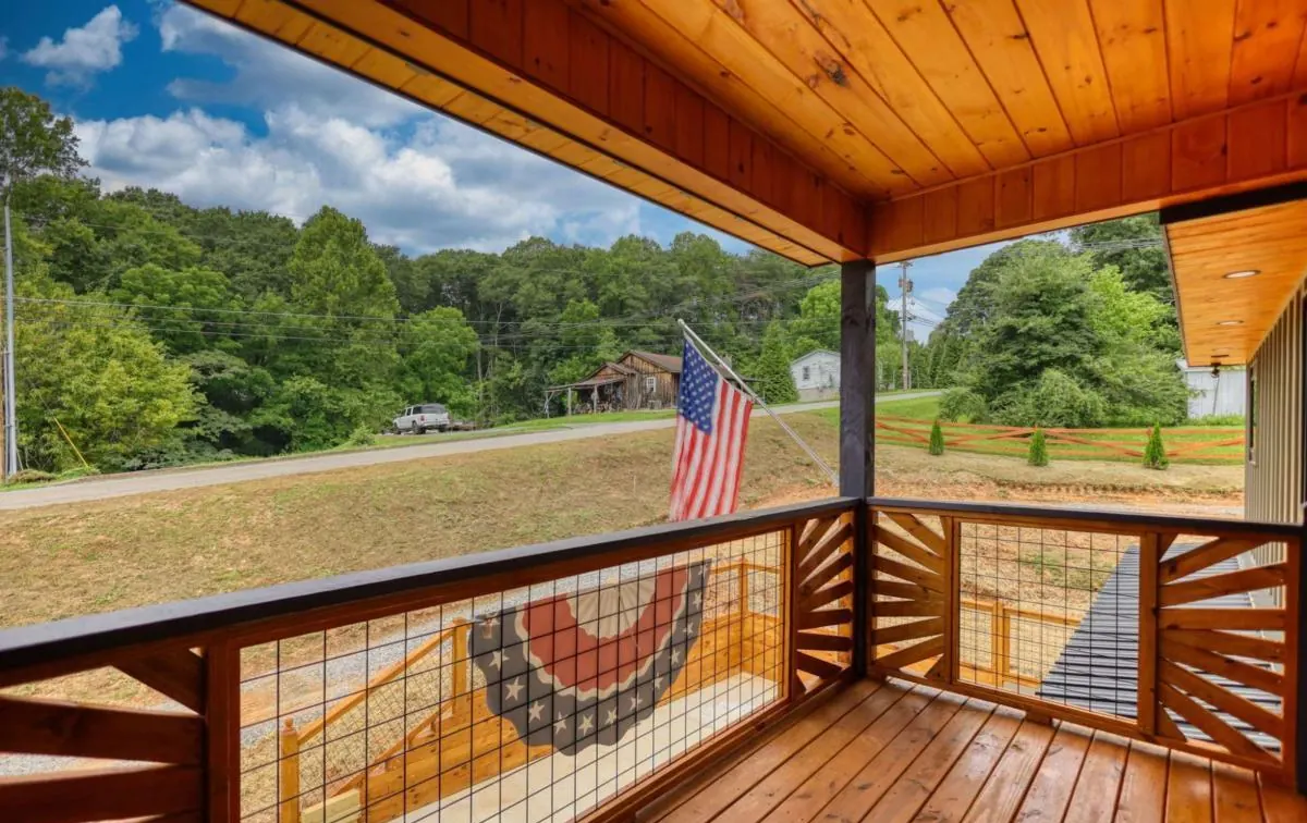 Porch railing with an American flag and a view across the yard to the trees
