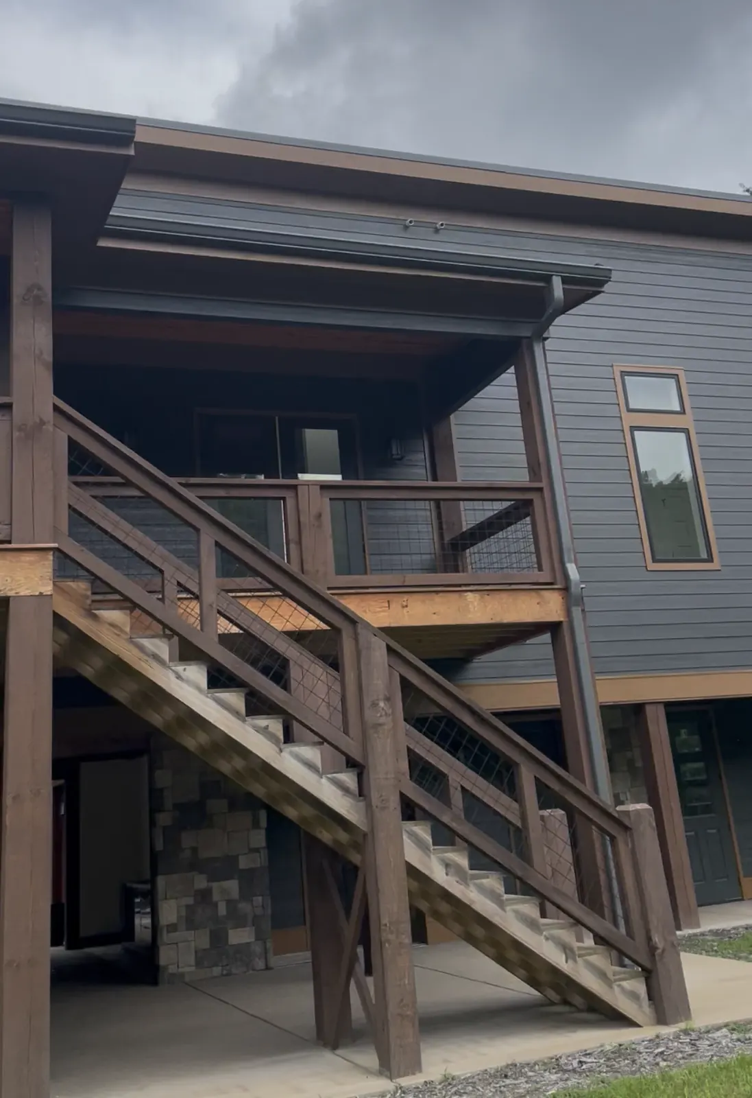 New two-story house with dark gray siding, a covered deck and wood stairs