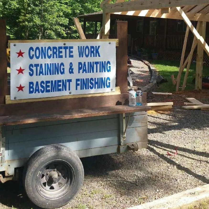 Company job sign on a trailer reading concrete work, staining and painting, basement finishing