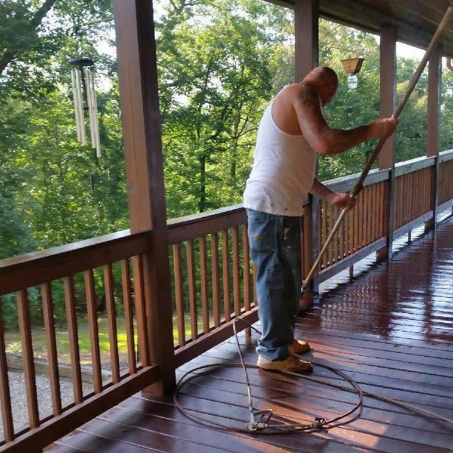 Crew member staining the deck boards of a covered log home porch