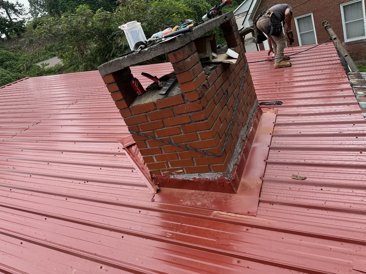 New red metal roof flashed around a brick chimney
