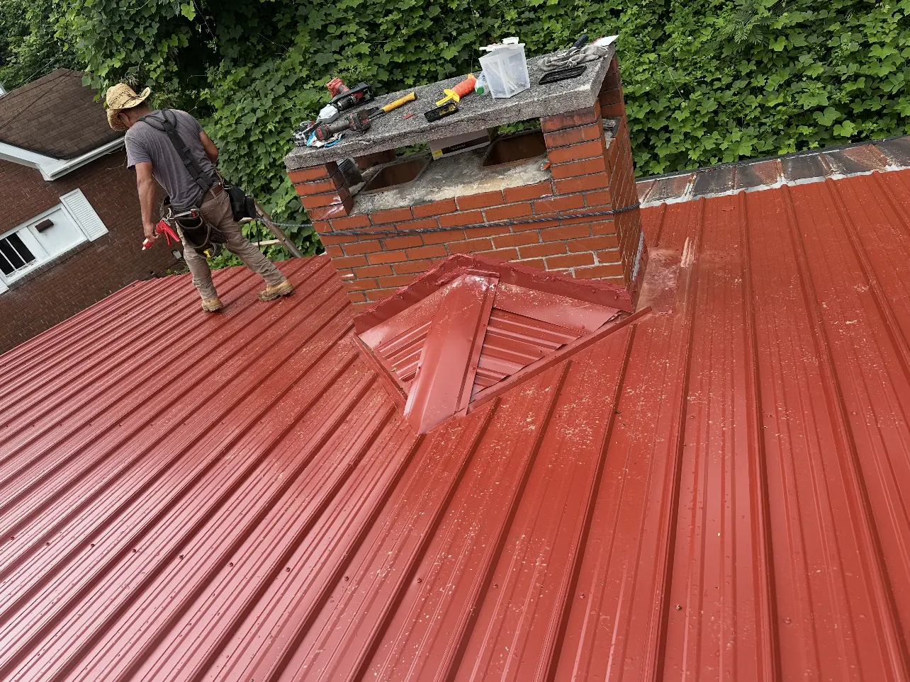 Crew at work on a new red metal roof around a brick chimney